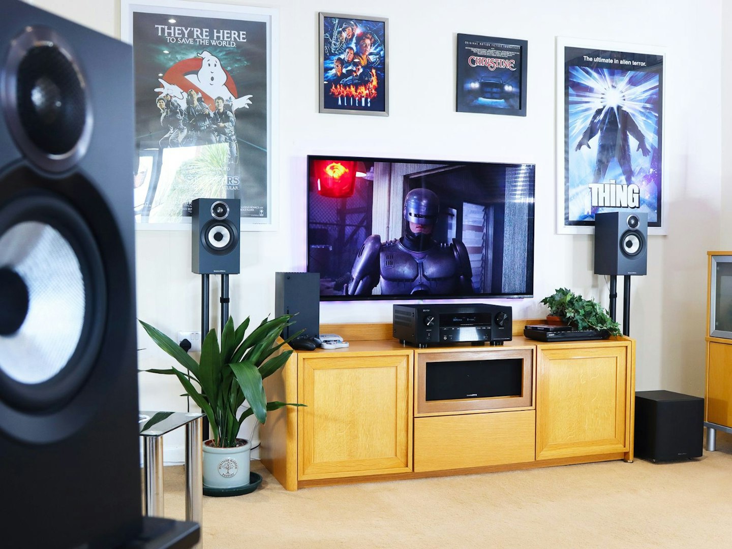 Denon AVR-X2800H Home Cinema Amplifier in a living room on a stand with Xbox and blu-ray player and speakers with a TV showing robocop