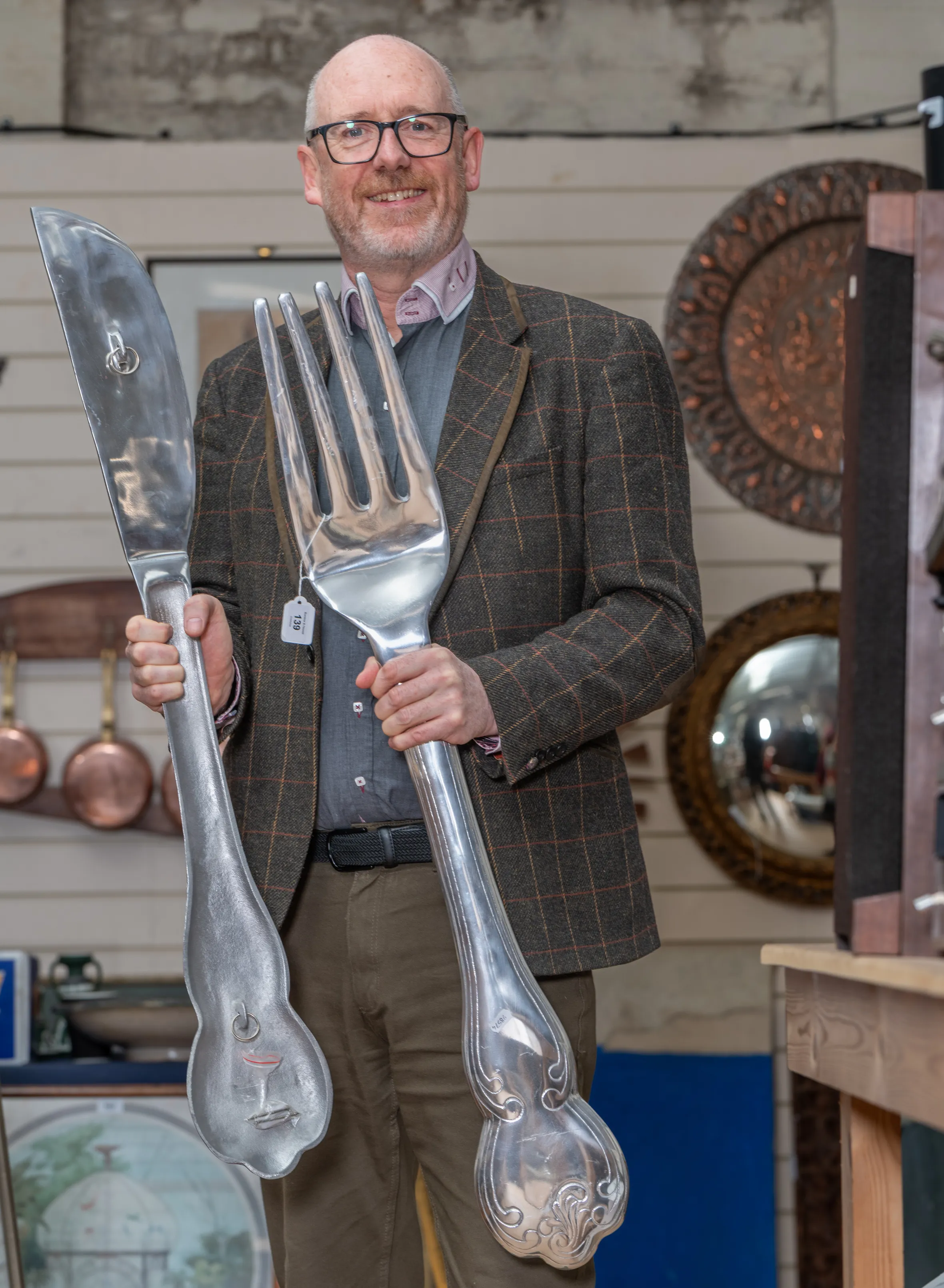 Mark Ellin, principal auctioneer at Burstow and Hewett auction house, holds up oversized decorative knife and fork.