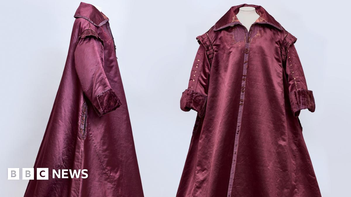 A side and front view of a 1600s era gown. It is a burgundy colour and has a collar.