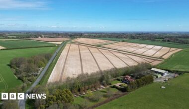 Aerial view of the proposed site near Beverley. It shows ploughed fields surrounded by hedges with a road running along the left. A farm with barns is at the bottom of the picture.