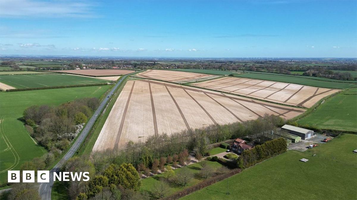 Aerial view of the proposed site near Beverley. It shows ploughed fields surrounded by hedges with a road running along the left. A farm with barns is at the bottom of the picture.