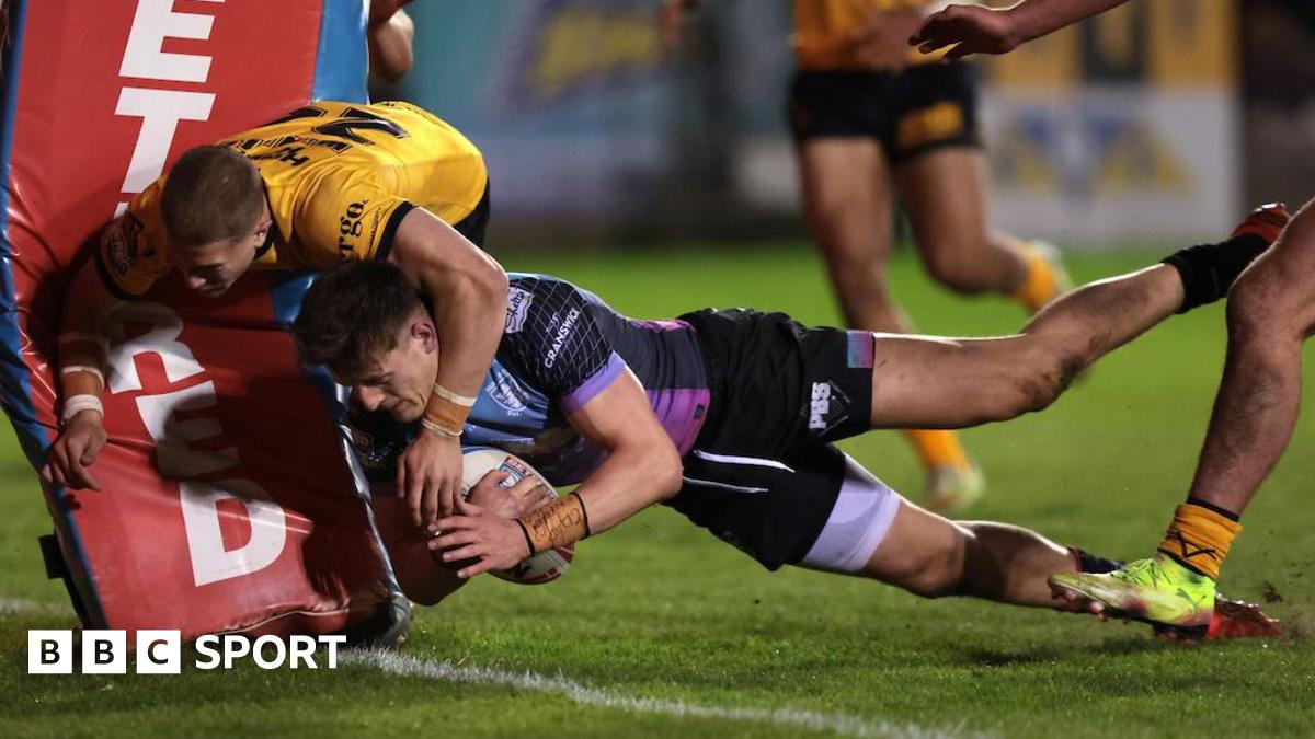 Hull FC's Davy Litten, in purple and blue shirt and black shorts, dives to score a try next to the post as Castleford Tigers' Jenson Windley, in black and amber, collides with the post while trying to stop him.