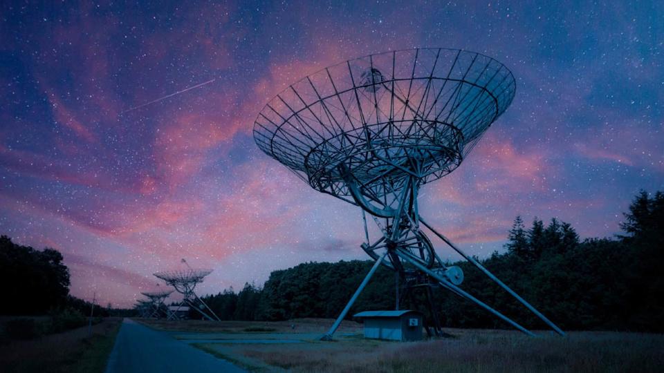 A row of satellite radars at night