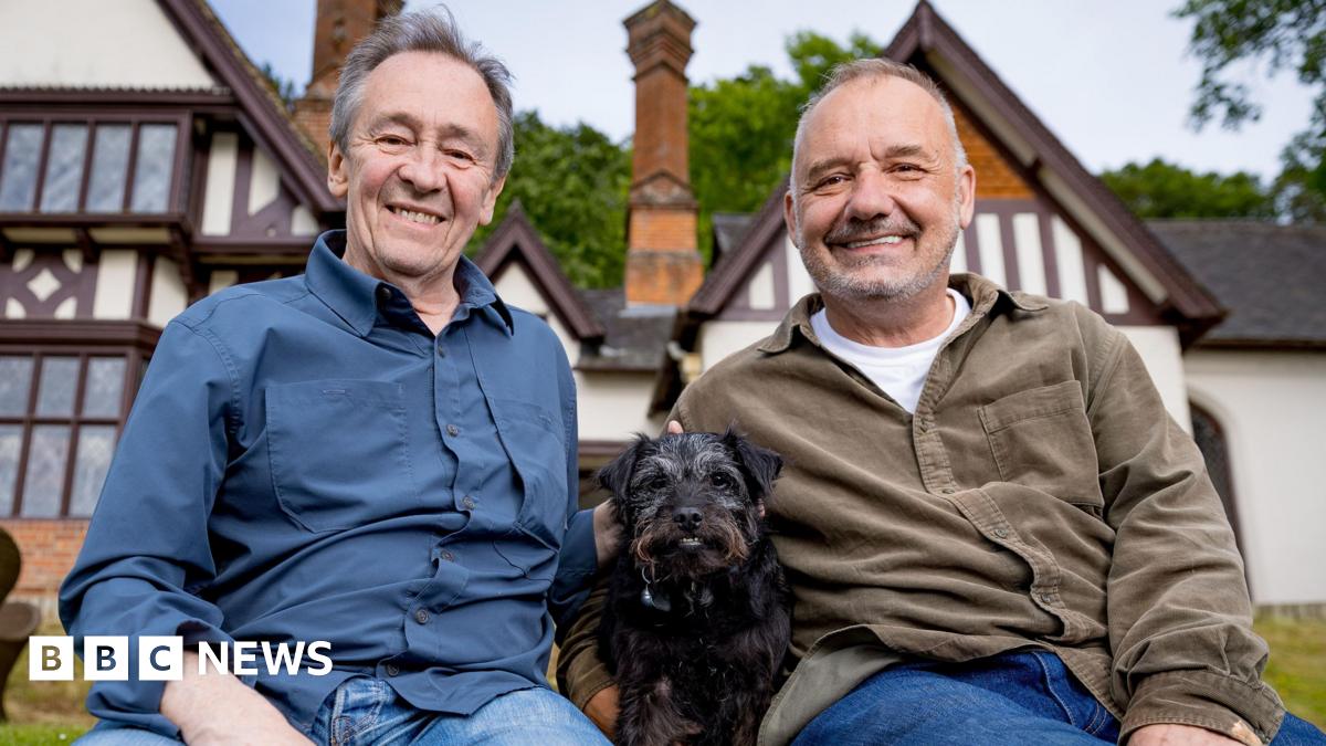 Bob Mortimer and Paul Whitehouse pose for a photo in front of a white house with black dog Ted in the middle.