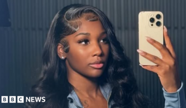 Ashly Robinson in a blue top, holding a phone as she takes a selfie of herself