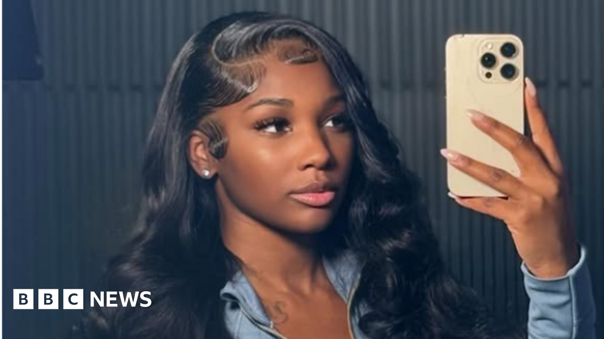 Ashly Robinson in a blue top, holding a phone as she takes a selfie of herself