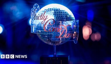 A person with their back to the camera wears a hi vis orange vest with the letters 'BMA' on the back, watching as resident doctors stand with placards while picketing outside Manchester university hospital on Tuesday.