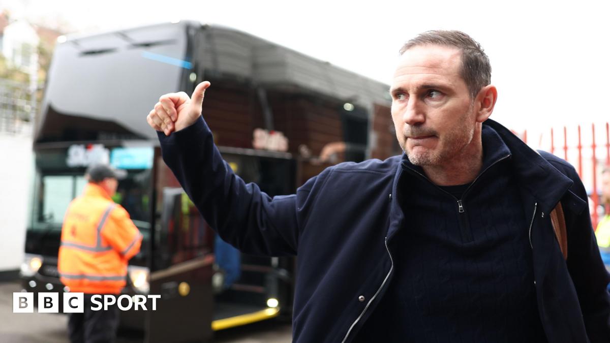 Frank Lampard gives a thumbs up in the direction of a bus outside a stadium.