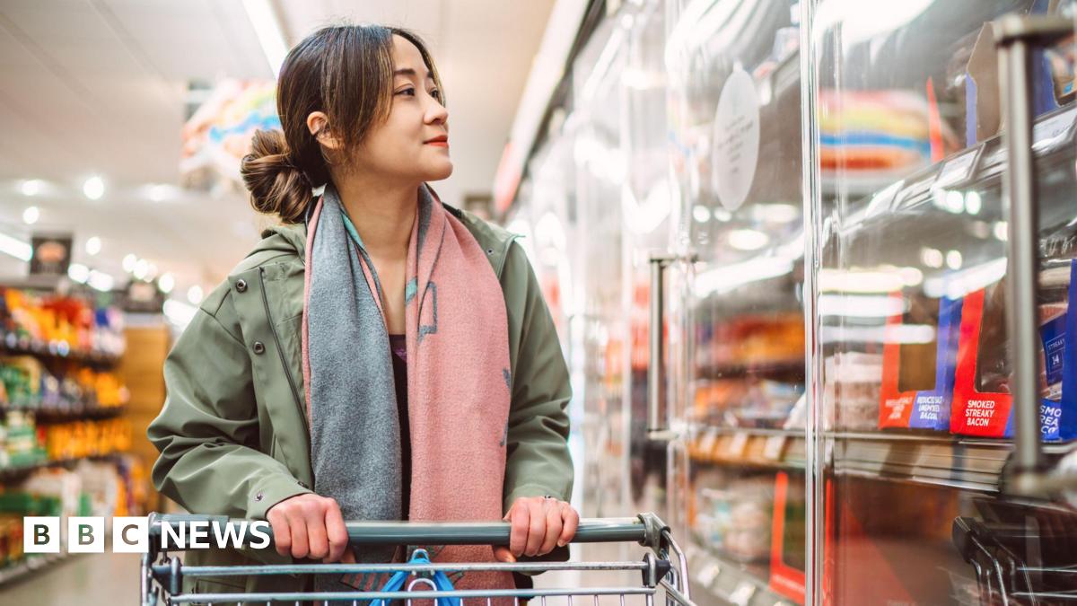 A woman holding a trolley in a supermarket looking to refrigerated shelves.
