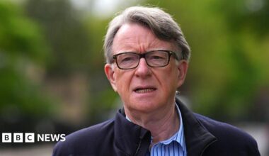 Lord Mandelson in glasses and a blue striped shirt