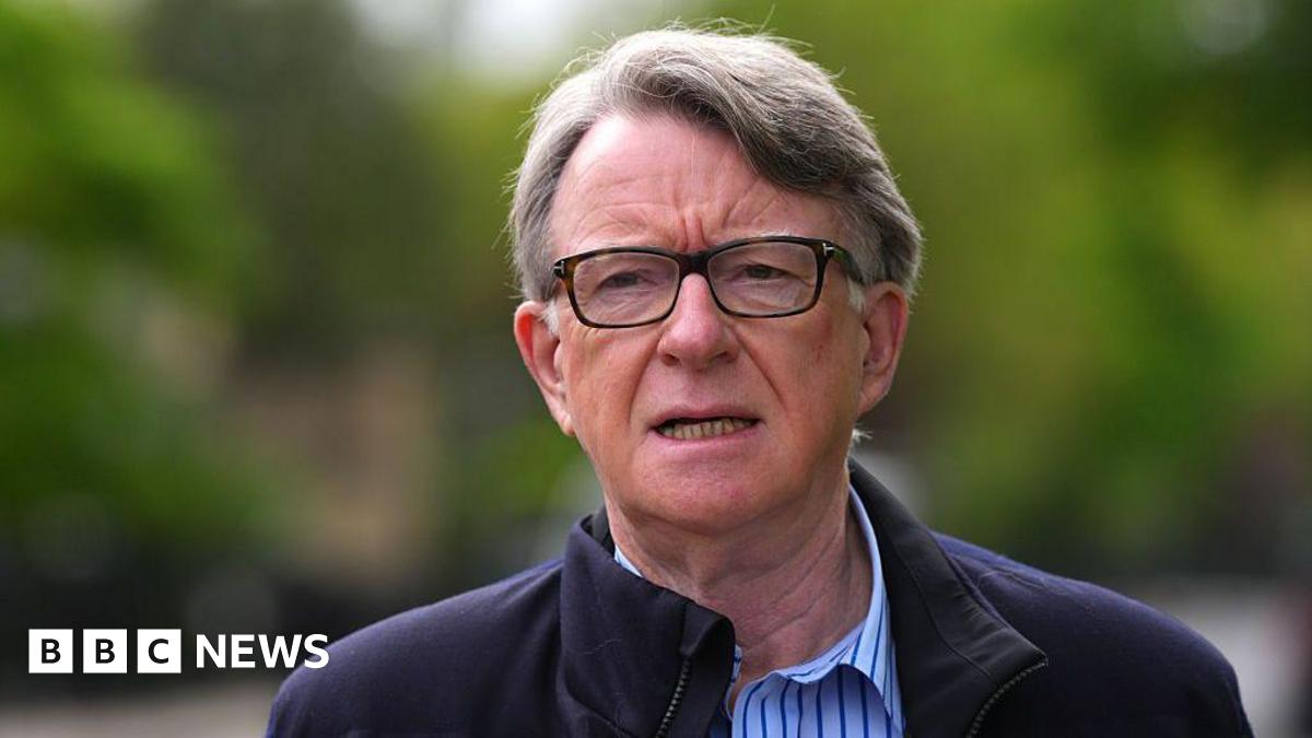 Lord Mandelson in glasses and a blue striped shirt