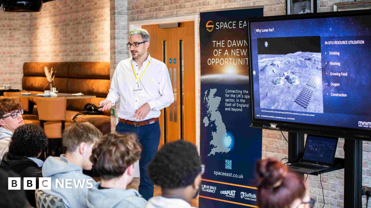 Andrew McCulloch, from Minima, giving a space engineering workshop to students at Suffolk New College. He is wearing a white shirt and navy trousers and addressing a group of students who are sitting down in front of him and a television screen.