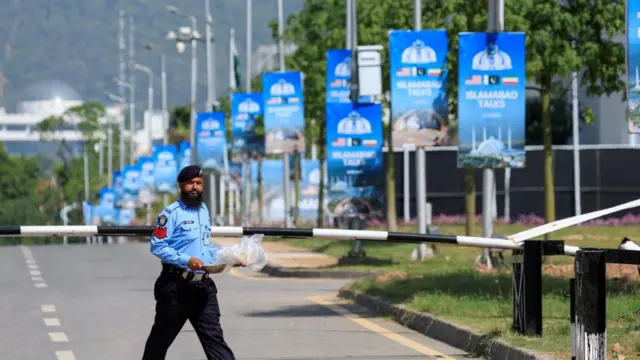 A security guard walks along an empty road, blue posters with white writing reading ISLAMABAD TALKS hang from several lamp posts