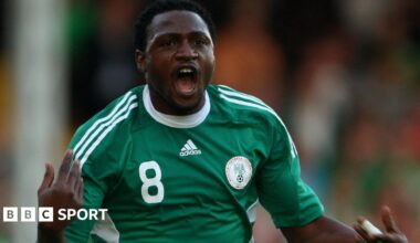 Michael Eneramo shown from waist up, wearing a green Nigeria shirt with white trim, the number eight on the right of his chest and Nigeria crest on the left, holds his hands up and is seen with his mouth open in celebration after scoring a goal