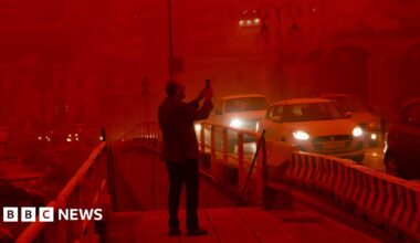 A man takes a picture while cars drive with their headlights on in red air.