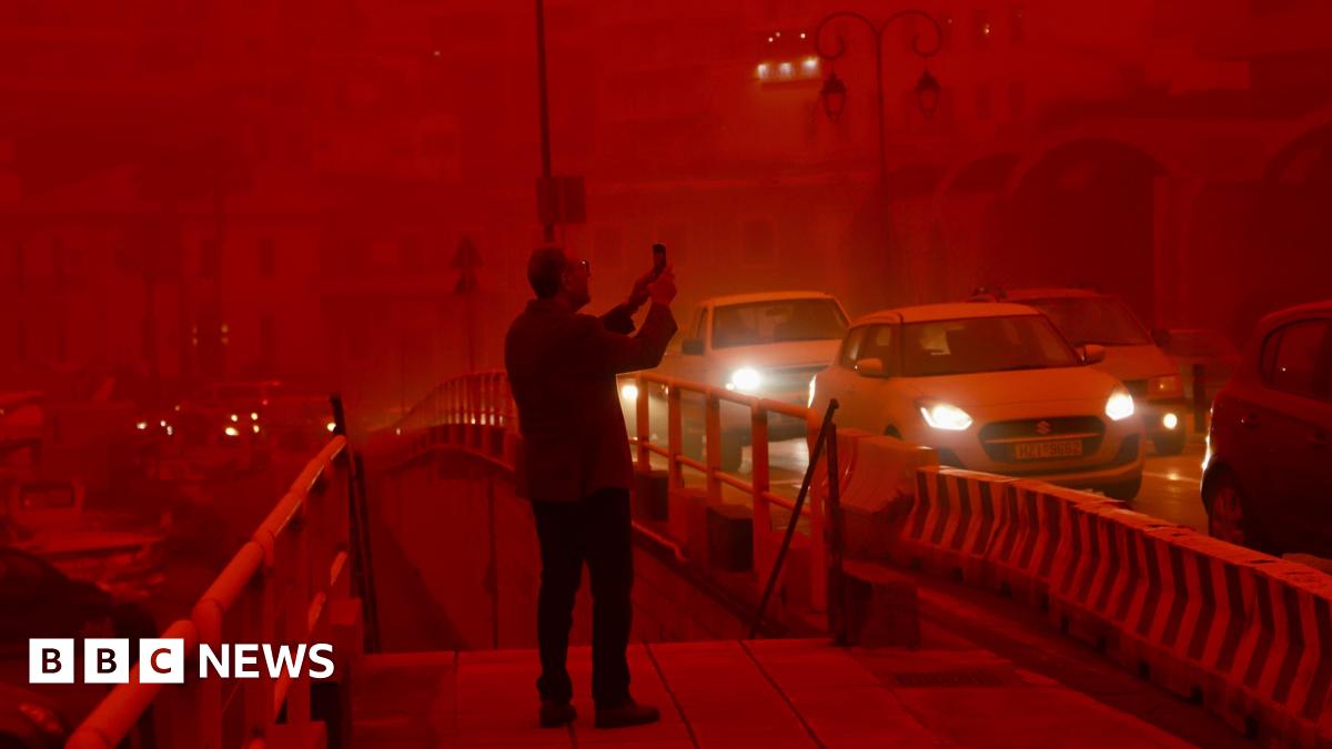 A man takes a picture while cars drive with their headlights on in red air.