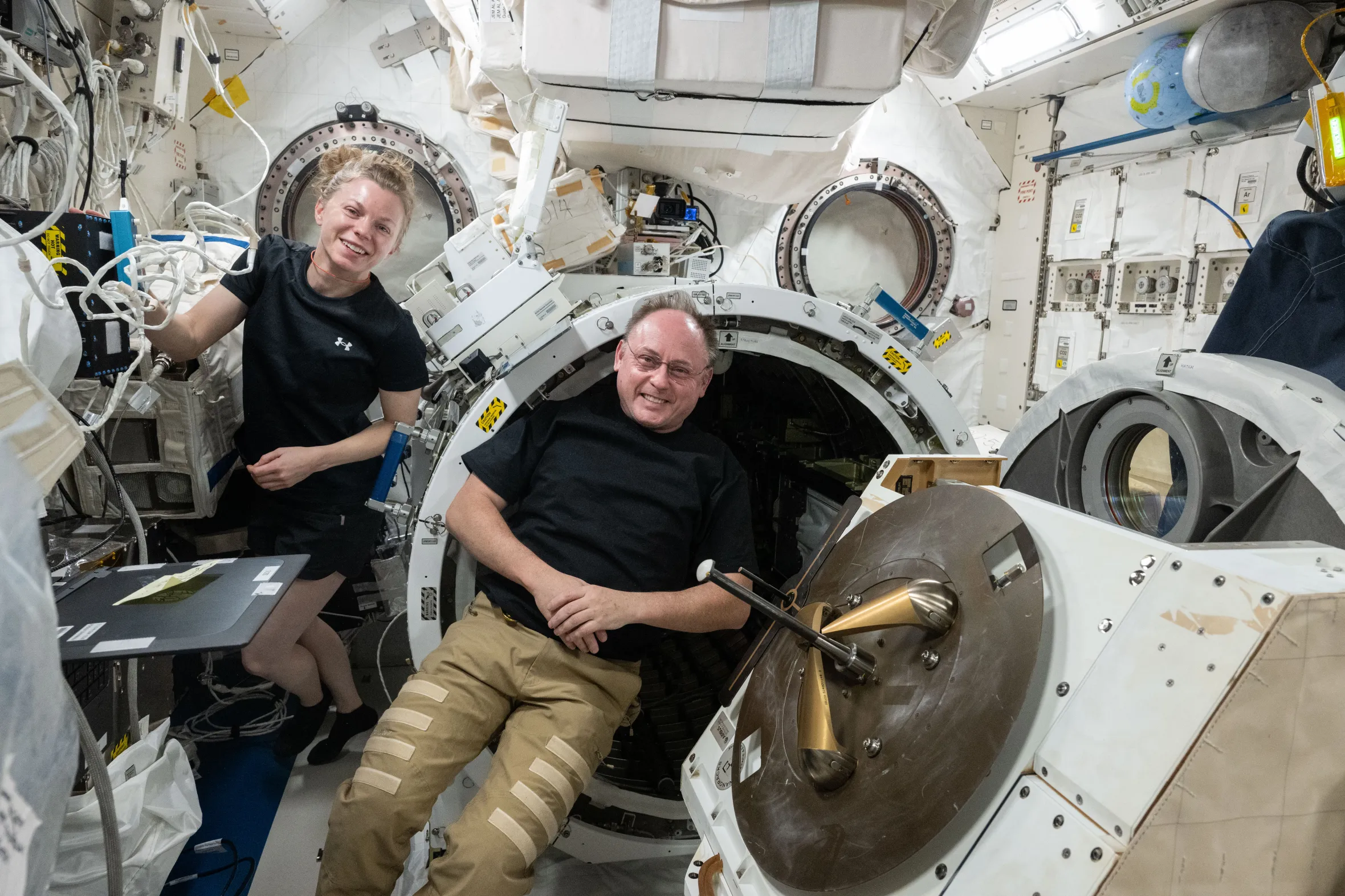 Astronauts Zena Cardman and Mike Fincke smiling during science hardware maintenance in the International Space Station's Kibo laboratory module.