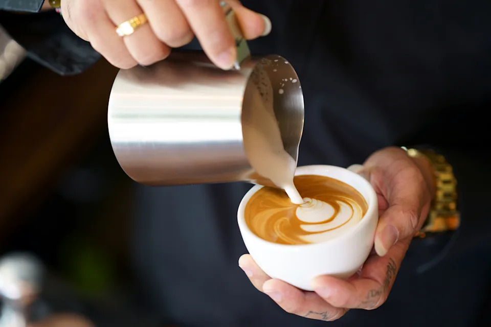 Barista hands pouring milk foam into of espresso resulting a pattern design on the surface on the surface of latte, Pouring Latte Art