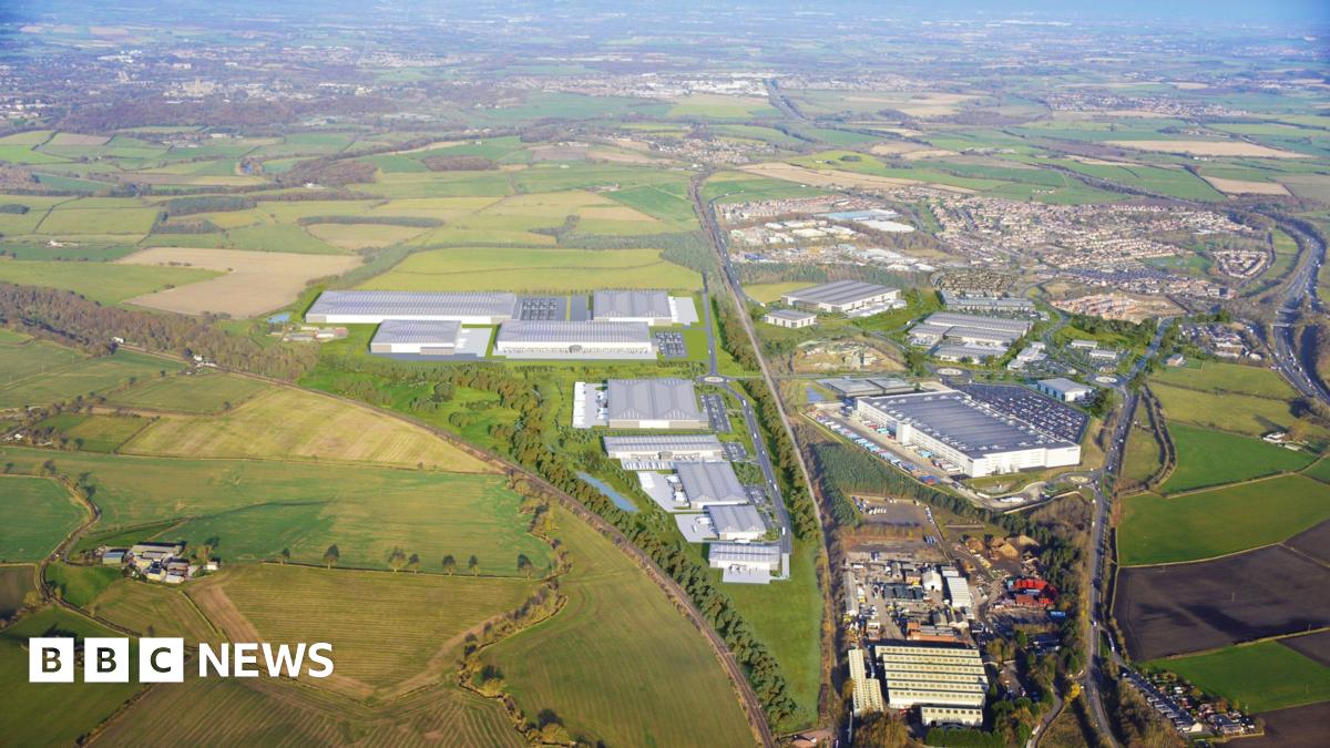 A computer generated image of the proposals shows large grey industrial units. A road separates the site from abother industrial sire and residential houses.