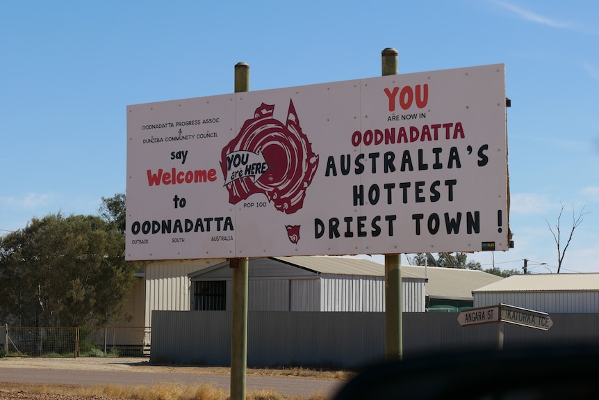 A sign in an outback town which says "Welcome to Oodnadatta, Australia's hottest driest town."