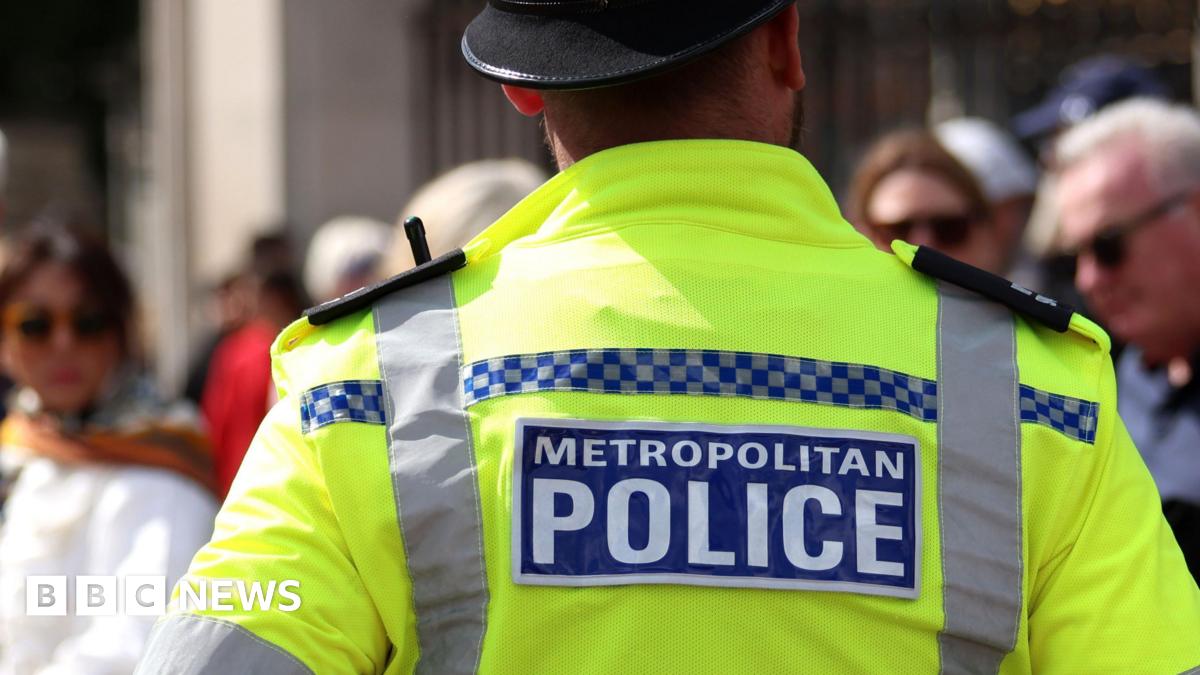 A Met Police officer with his back to the camera stands on a London street. There are passers-by slightly out of focus.