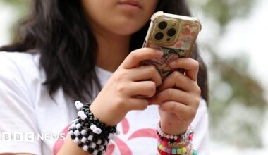 Close up image of an anonymous young girl wearing a white T shirt and colourful bead bracelets while using her smartphone outdoors, taken in Sydney in November.