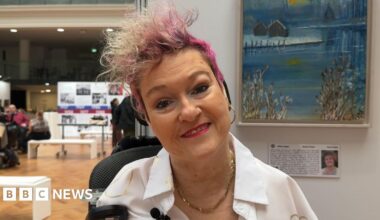 Woman smiling, head tilted and a painting on a wall