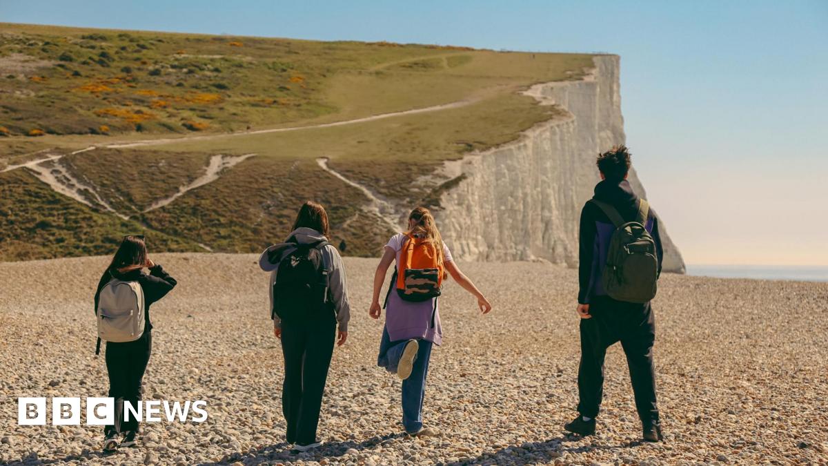Rear view of a group of hikers walking across a beach toward white cliffs on a sunny day