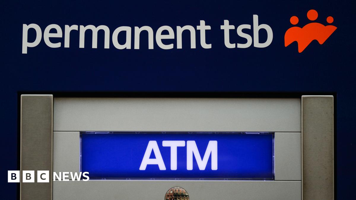 A close up of an atm. Lettering states permanent tsb ATM. A red logo shows three people. A reflection in a small circle shaped mirror displays a street.