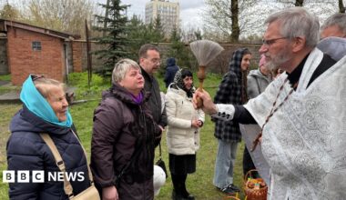 Priest dressed in a white robe giving his blessing to churchgoers.