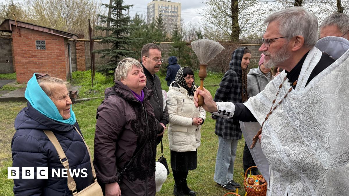 Priest dressed in a white robe giving his blessing to churchgoers.