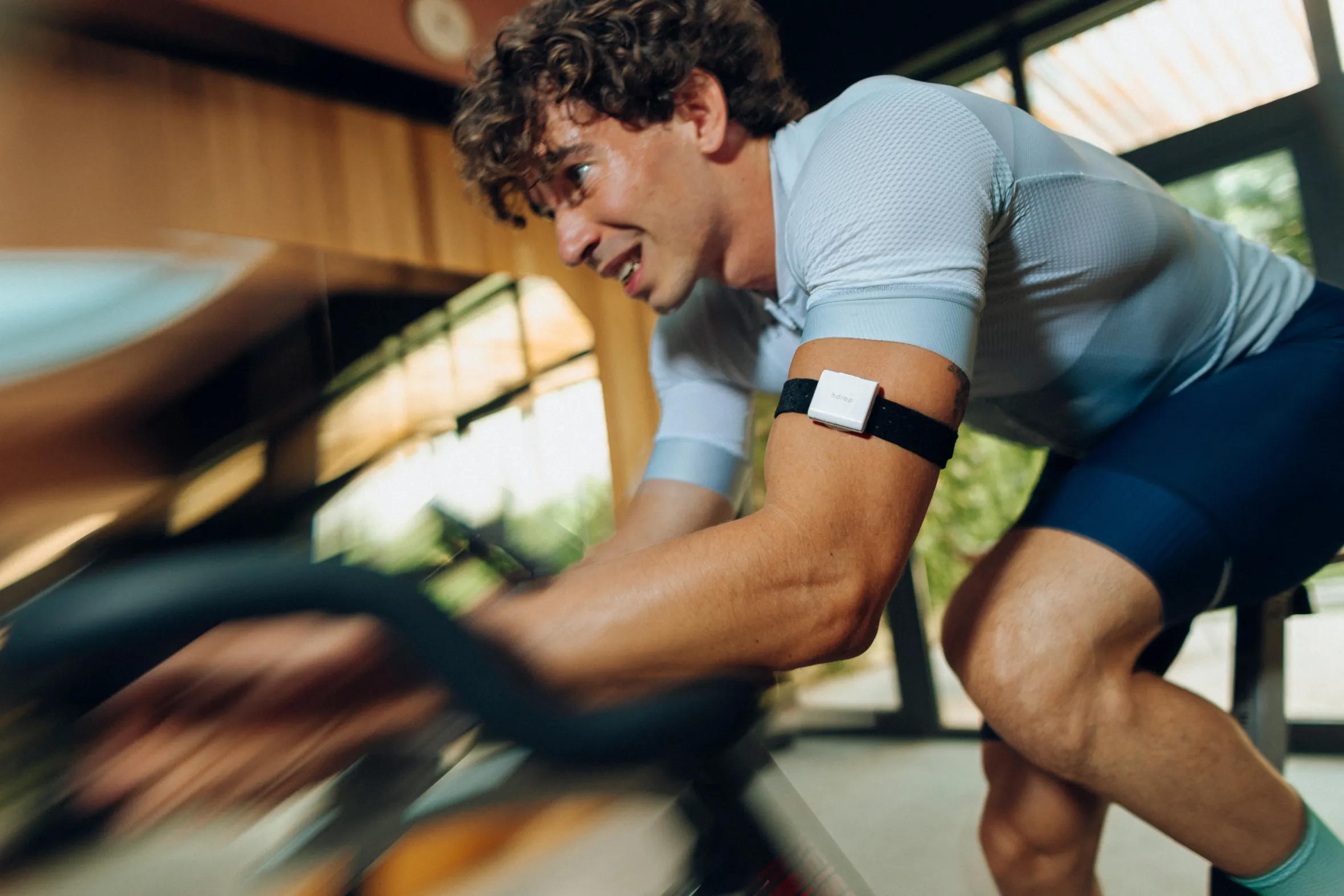 A man wearing a hDrop wearable hydration monitor on his arm while exercising on an indoor bicycle.