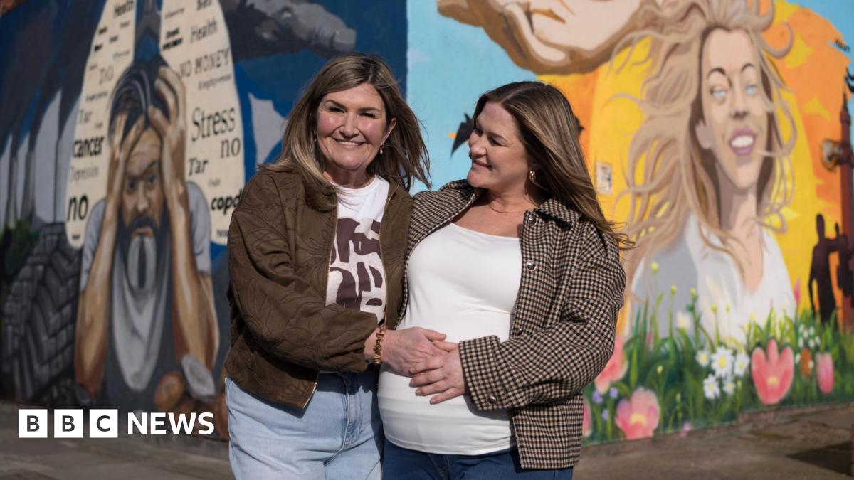 Wendy Robinson pictured with her daughter Amy standing in front of a colourful mural on two sides of a wall. Amy, on the right, has blonde hair and is smiling. There are blue skies, sun, flowers and birds behind her. On the mural towards the left is a picture of a man holding his head in his hands with words including 'cancer, stress, no, health' written in a lung-diagram on a dark blue background.