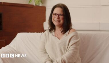 Paula Van Santen smiling for an image in a room. She is sitting down on a cream couch and is wearing a cream top.