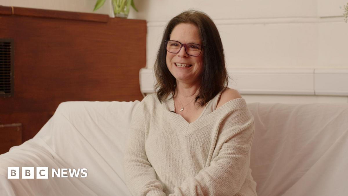 Paula Van Santen smiling for an image in a room. She is sitting down on a cream couch and is wearing a cream top.