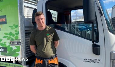 Jacob Francis standing in front of the driver's door of a large white van. His hands are behind his back. His hair is short and brown and he is wearing a khaki t-shirt.