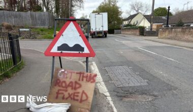 Road with a pothole and a sign calling for the road to be fixed