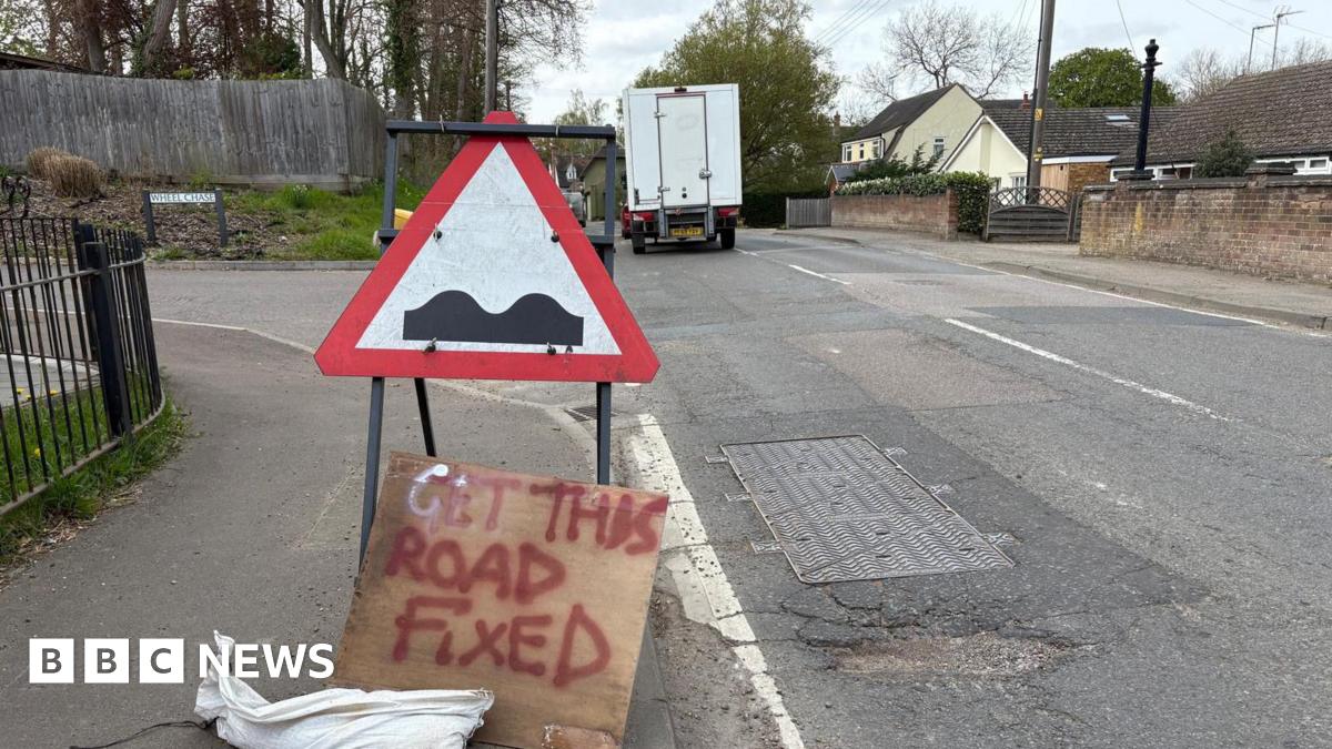 Road with a pothole and a sign calling for the road to be fixed