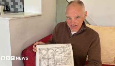 A man is sitting on a red sofa with a yellow cushion behind him holding a hand drawn picture of Knaresborough Viaduct