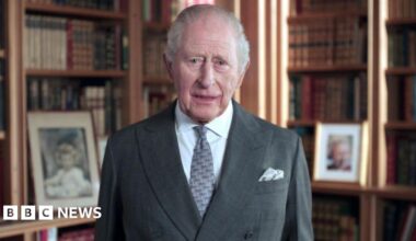 King Charles in a suit and tie with bookcases in the background
