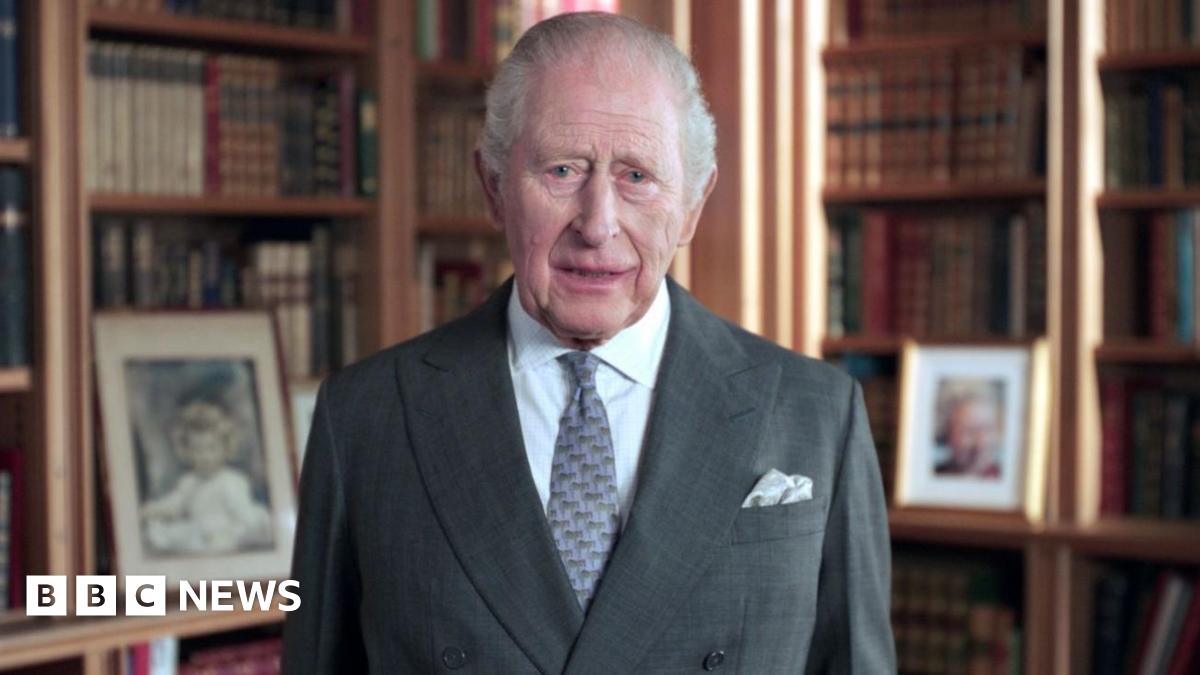 King Charles in a suit and tie with bookcases in the background