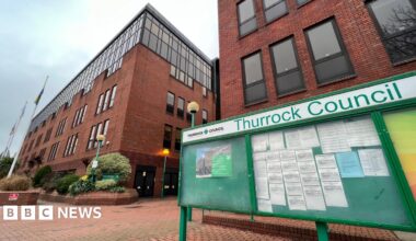 The outside of Thurrock Council's red brick offices. A green notice board with three panels stands in the foreground.