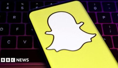 A smartphone showing Snapchat's logo, a white, faceless ghost figure on a yellow background, in front of a keybaord.