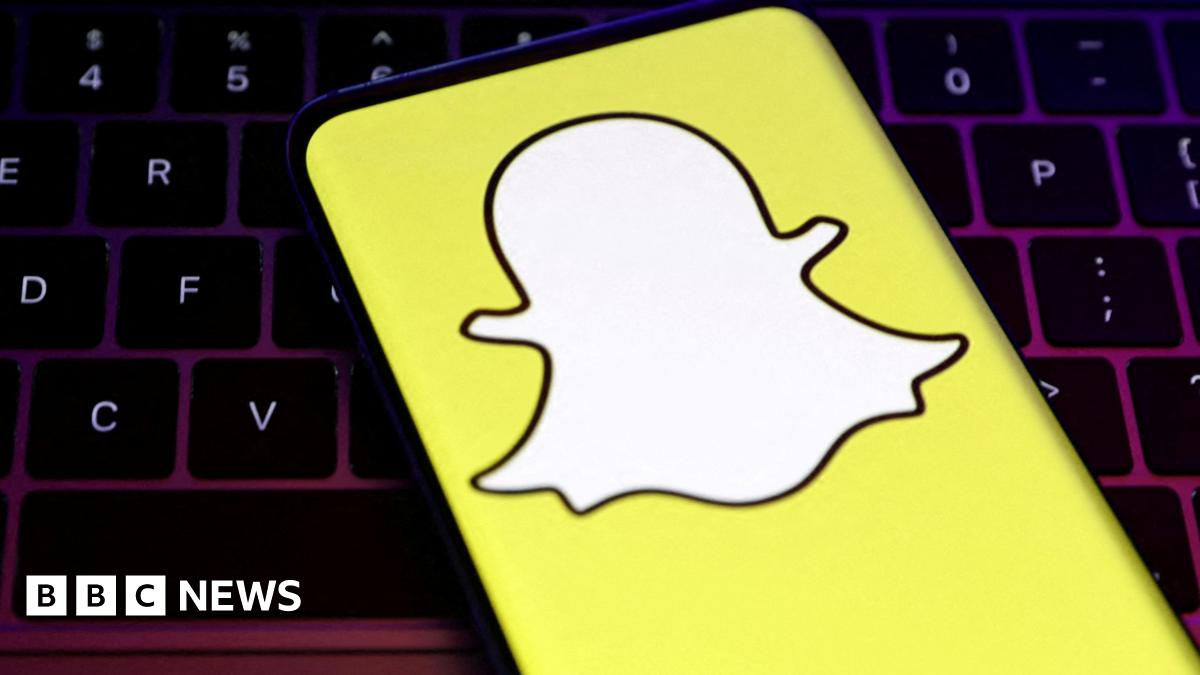 A smartphone showing Snapchat's logo, a white, faceless ghost figure on a yellow background, in front of a keybaord.