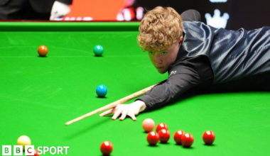 Stan Moody stretches over the snooker table to play a shot