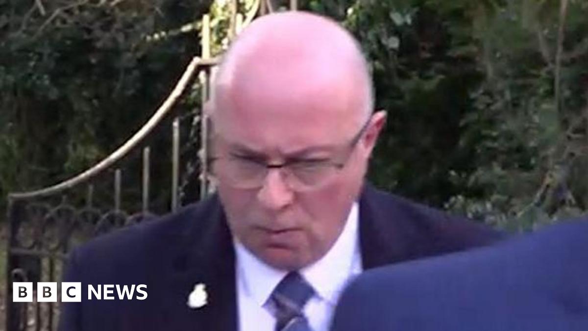 PC Mark Roberts leaving Durham Crown Court. He is wearing a dark suit and a blue striped tie. He is bald, wearing glasses and looking down.