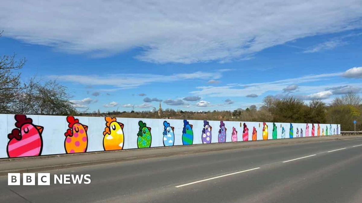 A mural on a wall at the side of a road shows paintings of chickens in various colours