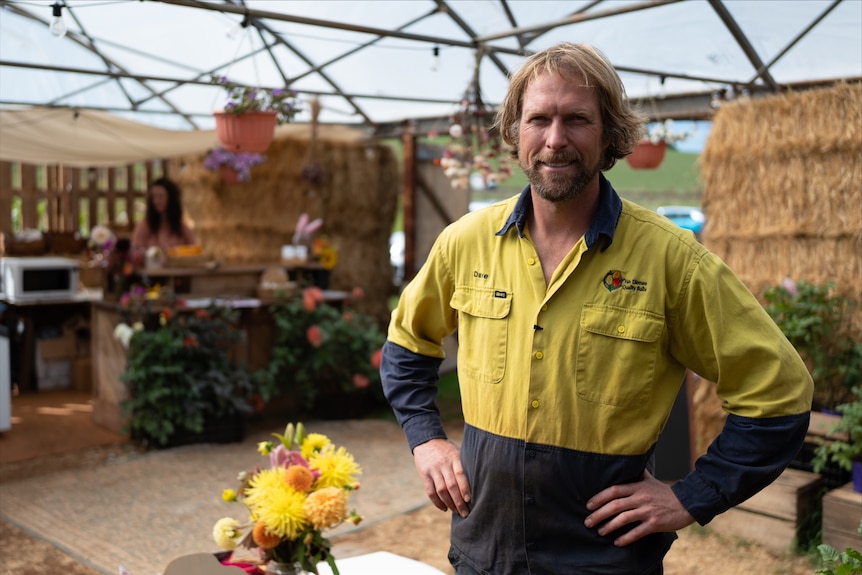 A man in a yellow Hi-Vis shirt stands in front of a few bales of hay.