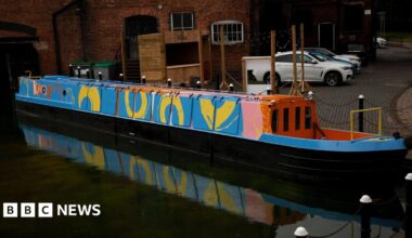 A canal boat which is painted blue with yellow circles, pink pint strokes and has a red and orange hull