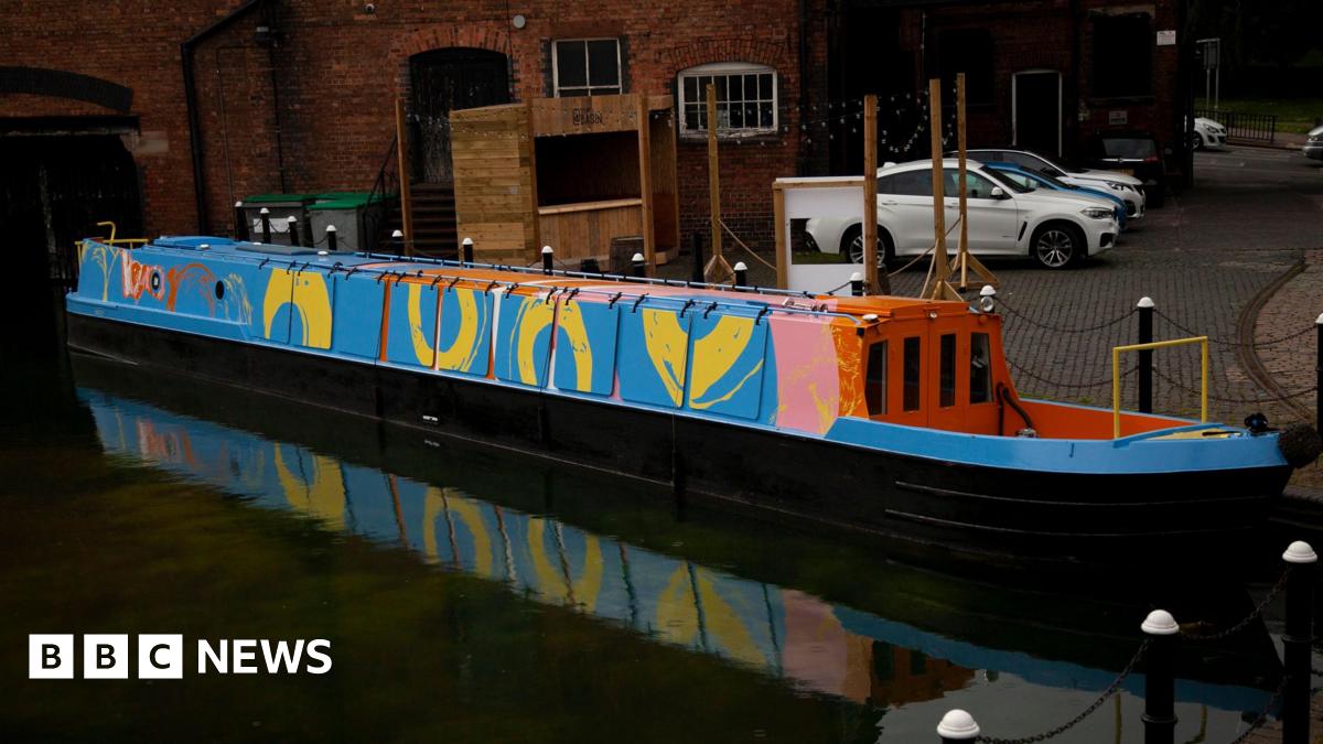 A canal boat which is painted blue with yellow circles, pink pint strokes and has a red and orange hull
